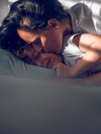 Mother kissing sleeping son on bed