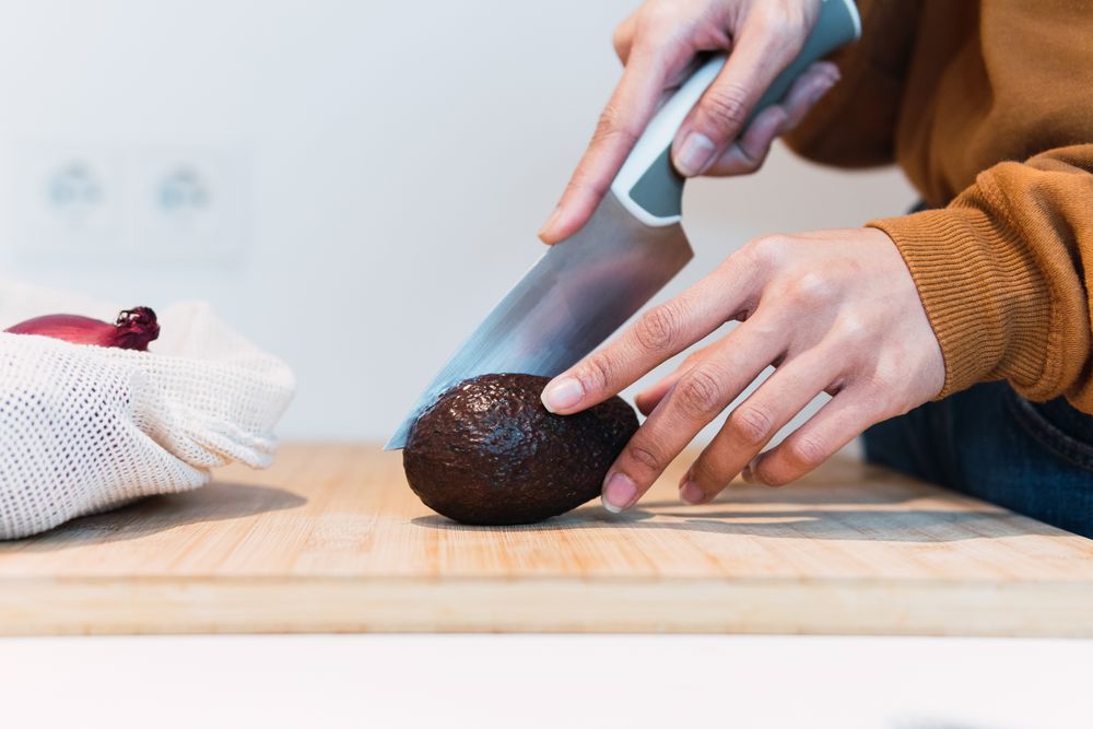 Crop woman cutting avocado in kitchen
