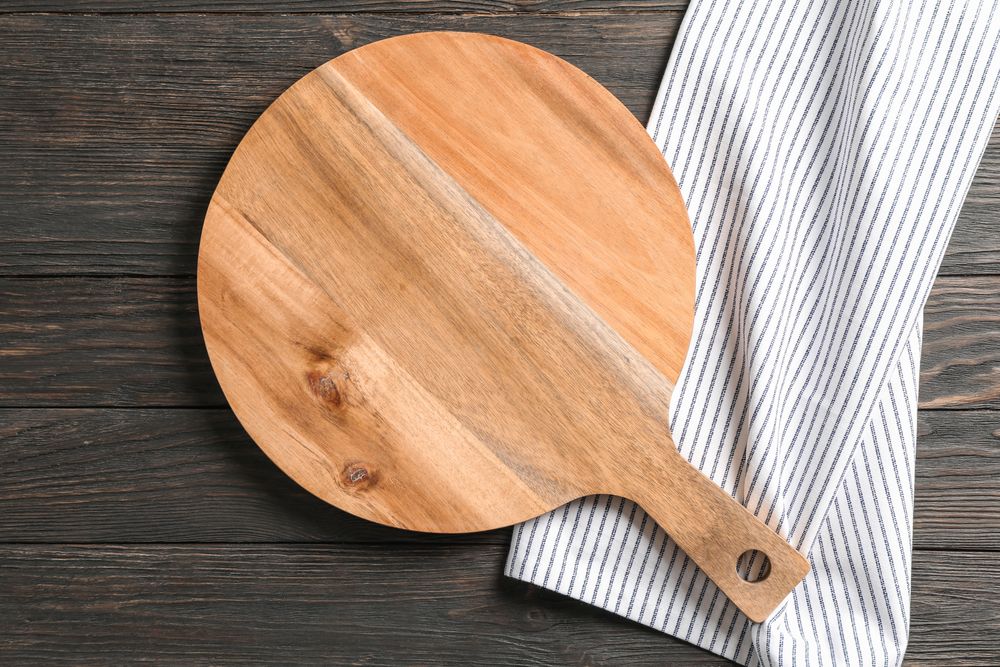 Cutting board with kitchen towel on wooden background, space for text