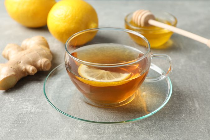 Cup of tea, lemon, honey and ginger on grey background, close up