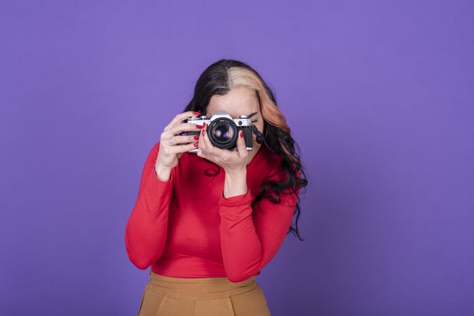 woman taking a photo with her film camera over a violet background.
