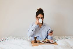 Young woman with breakfast on bed using smart phone