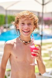 Shirtless boy smiling and holding drink at resort