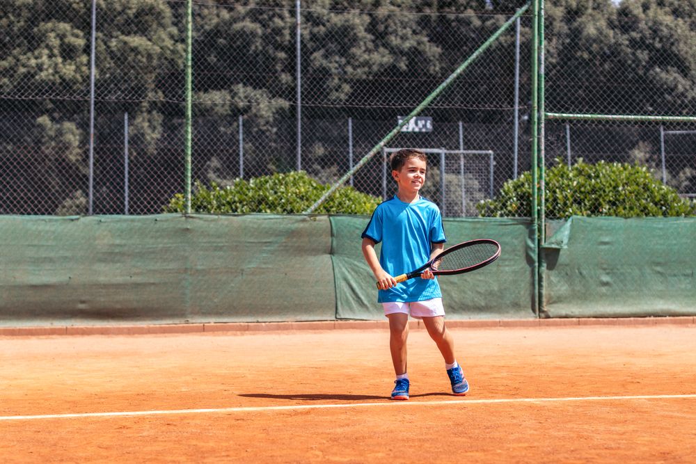 Little boy playing tennis on a dirt court