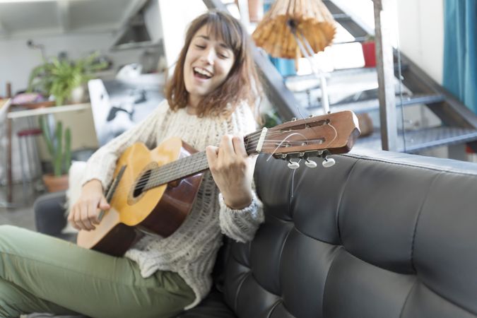 Female on sofa playing acoustic guitar and singing at home in living room