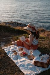 Woman reading on mat for picnic on seashore
