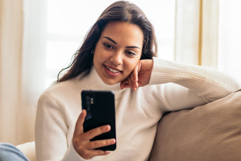 Connected at Home: Young Woman Sitting on Sofa Using Smartphone