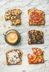 Toasts with bites taken out, with different fresh fruit toppings on marble counter, with coffee