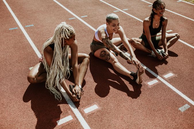 Three female athletes sitting on a running track and stretching legs