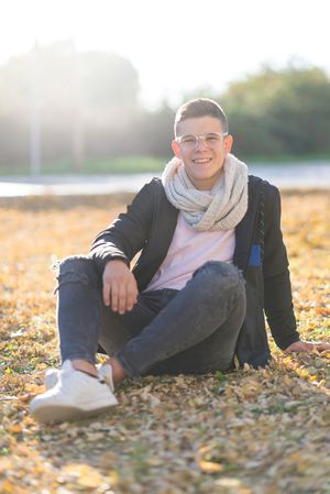 Smiling teenage male in striking eyewear sitting in a city park