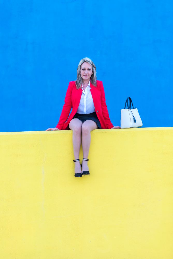 Woman in red coat sitting on bright yellow wall with blue in background