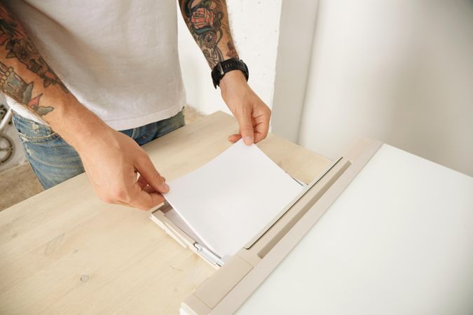 Man with tattoos refilling paper tray of printer