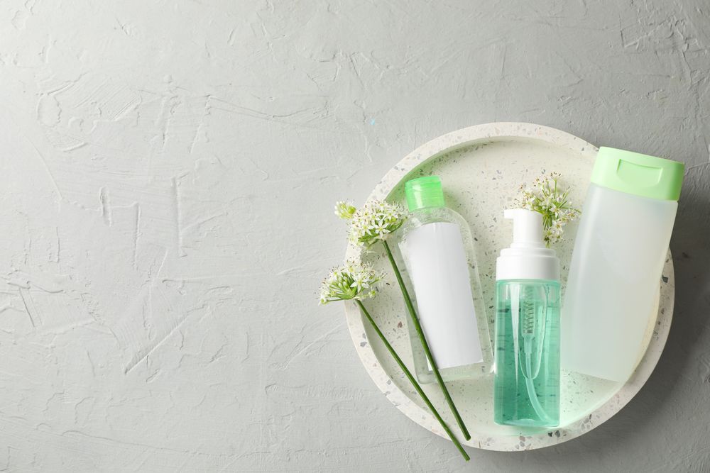 Liquids for body care in different bottles and allium flowers on plain background