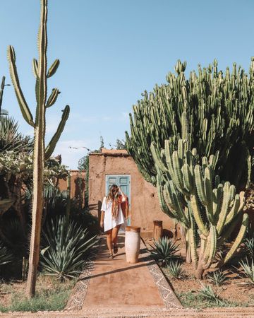 Woman standing beside house and cactus trees
