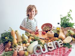Adorable boy cutting tomato on chopping board near assorted veggies