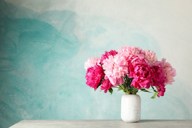 Vase with bouquet of beautiful peonies on grey table against blue background, space for text