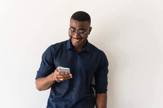 Happy Black guy with phone and laptop near wall