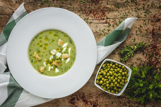 Green vegetable cream soup with crackers and peas in bowl