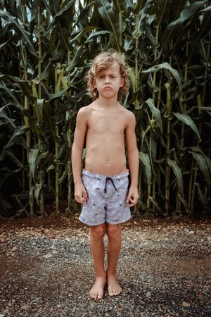 Displeased boy standing against green corn plantation