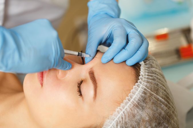 Cosmetologist at med spa injecting botox into forehead wrinkles in female client