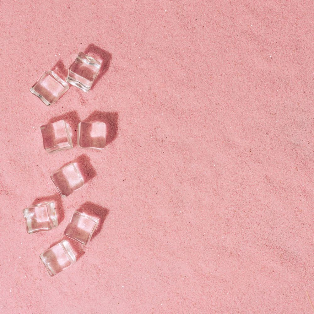 Flat lay of ice cubes on pink sand background with shadows