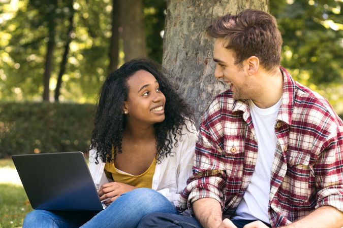 Multiracial couple studying in the park with laptop