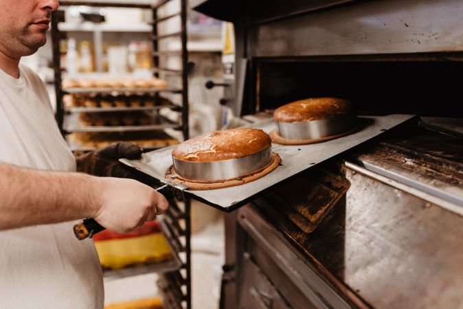 Bald baker checking pastry inside oven