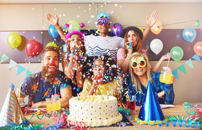 Friends with confetti, novelty glasses, drinks and cake at birthday party