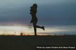 Silhouette of woman with her leg kicked up behind her in a field at dusk 0LdkR0