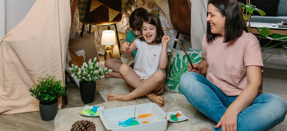 Happy mother and daughter camping at home playing diy fishing ga