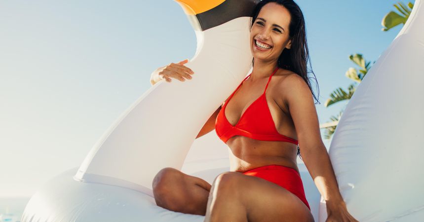 Pretty female wearing a red bikini and sitting on inflatable swan