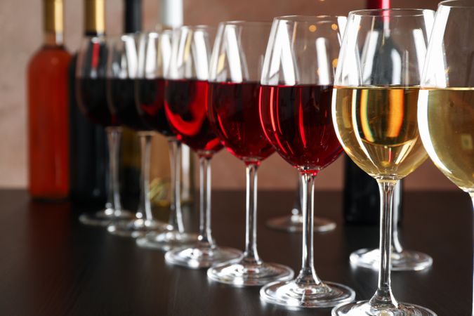 Bottles and glasses with wine on dark table, blurred lights, closeup