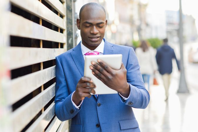 Male standing with a digital tablet on street while leaning against wall