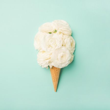 Waffle cone with fresh flowers  on a pastel green background, square crop