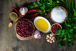 Top view of bowls of kidney beans, oil, pepper, garlic bulb, cilantro and onions