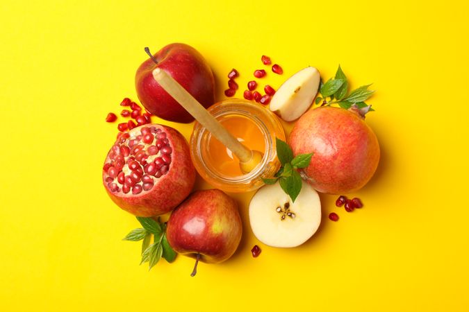 Top view of fresh apples, pomegranate and honey grouped in centered on yellow background