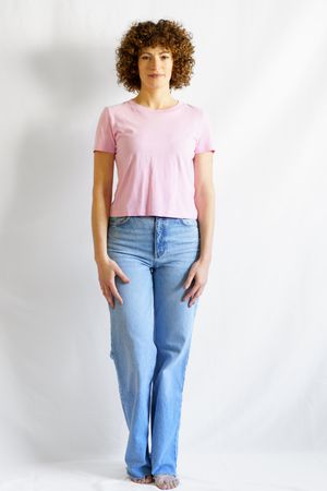 Woman in pink t-shirt and jeans standing barefoot in bright studio facing forward