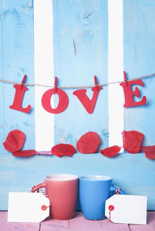 Two mugs with labels and the word love spelled out in paper letters hanging on a fence behind