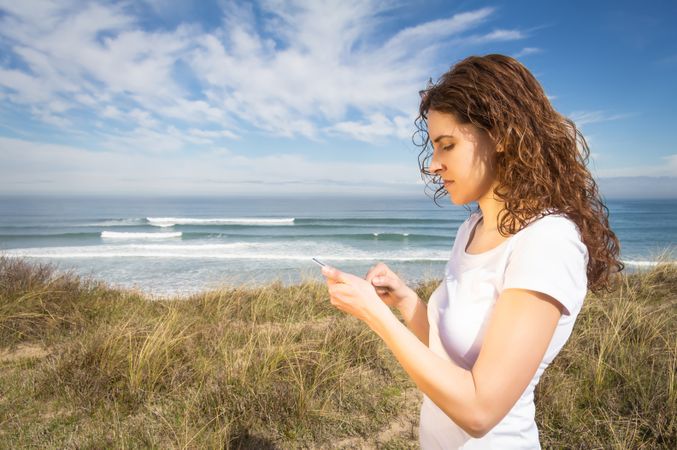 Side view of woman checking phone with ocean waves in background