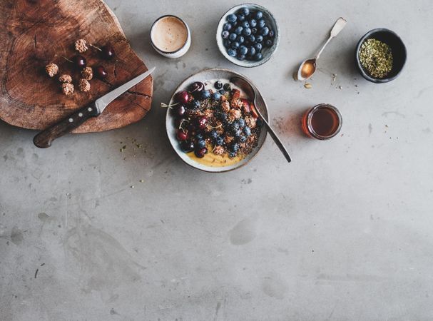 Oat granola yogurt bowl with cherries, blueberries, honey, nuts, coffee, wooden board