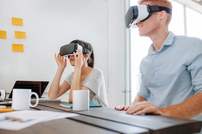 Young man and woman sitting at a table and using virtual reality goggles