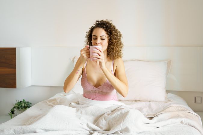 Woman in nightwear drinking fresh coffee in bed