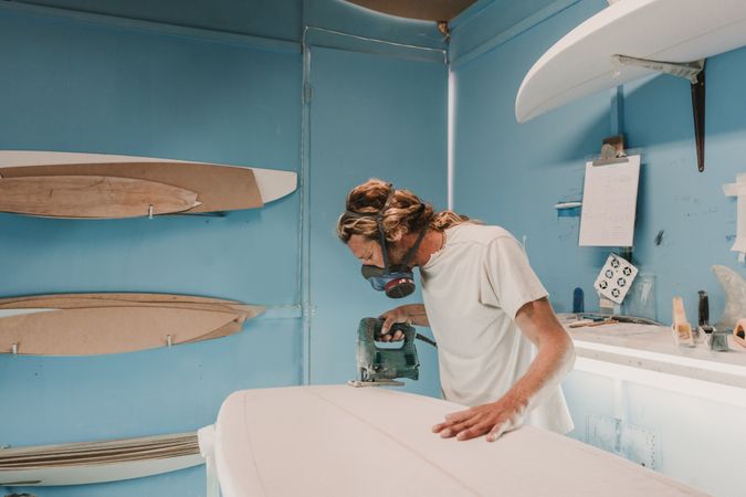 Man with tool sawing surf board in workshop