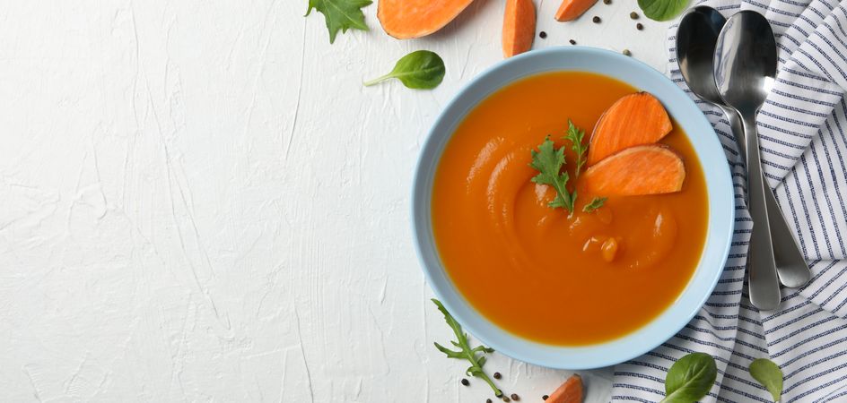 Wide shot of bowl of sweet potato soup on table with salt pepper and spoons with copy space
