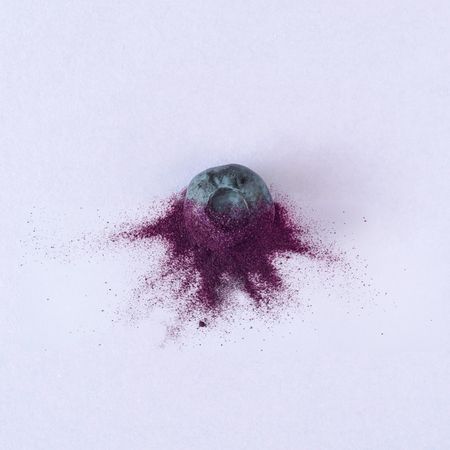 Single blueberry with purple dust on purple background