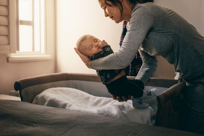Woman bending forward to put her infant kid in a bedside bassinet