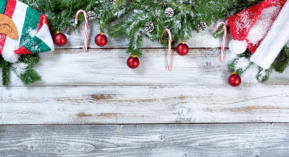 Snowy Christmas fir branches along with traditional hats and ornaments on rustic wooden background