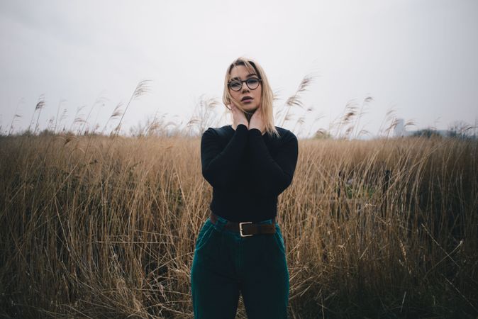Young attractive blonde female model with glasses posing in wheat field on cloudy day