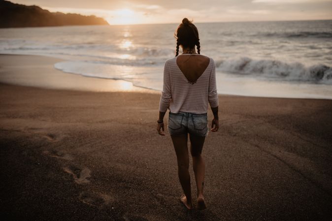 Anonymous female walking towards waving sea on sunset