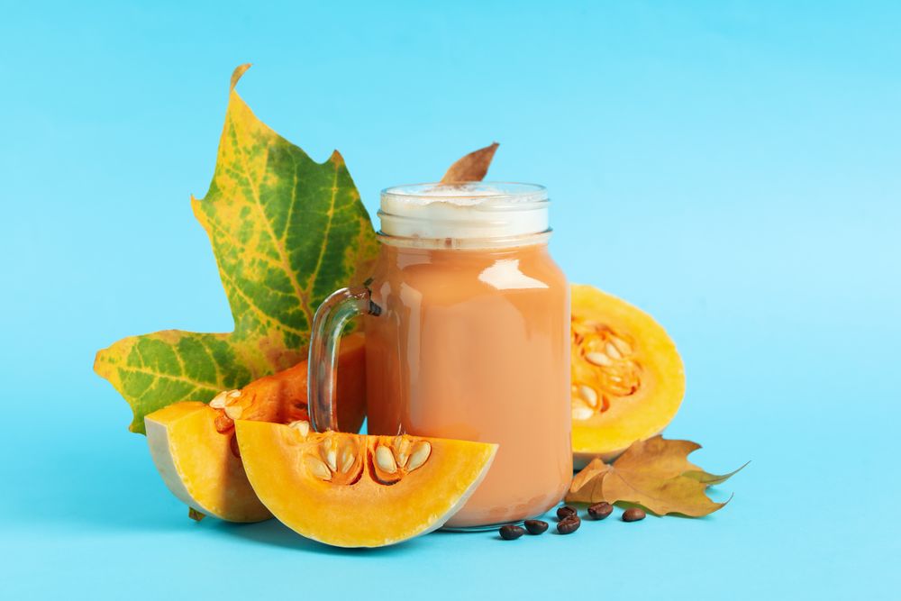 Composition with glass jar of pumpkin latte on blue background